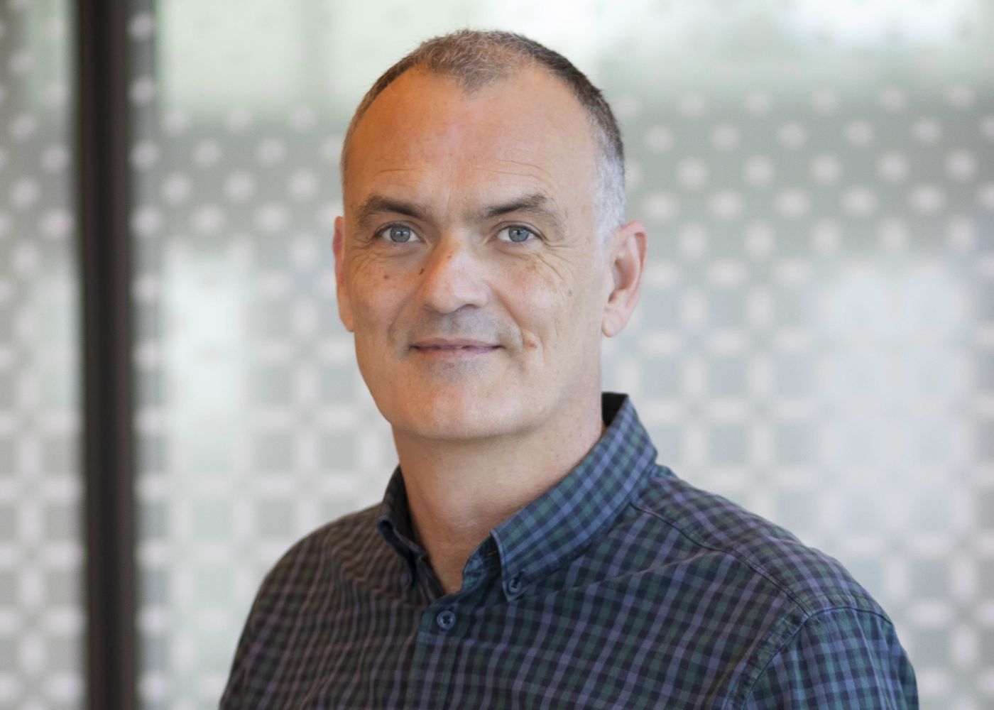Penington Institute CEO John Ryan standing against glass background.