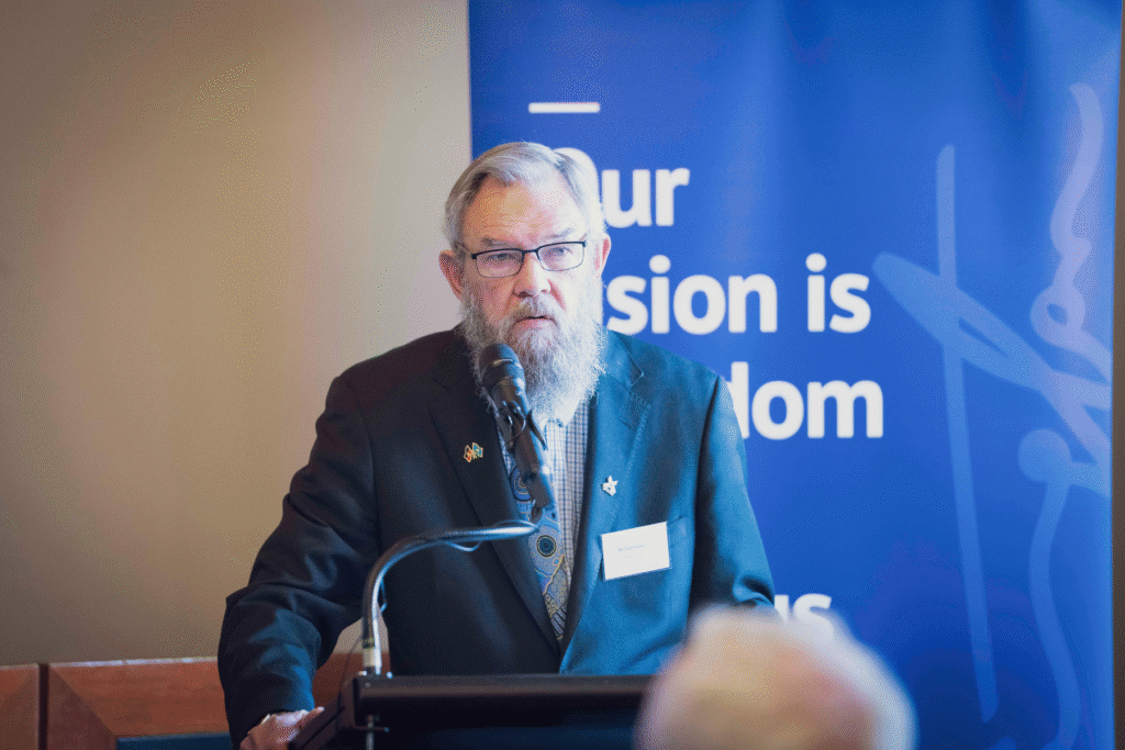 Penington Institute Chair Scott Wilson addresses audience at lectern and mic
