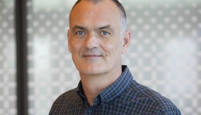 Penington Institute CEO John Ryan standing against glass background.